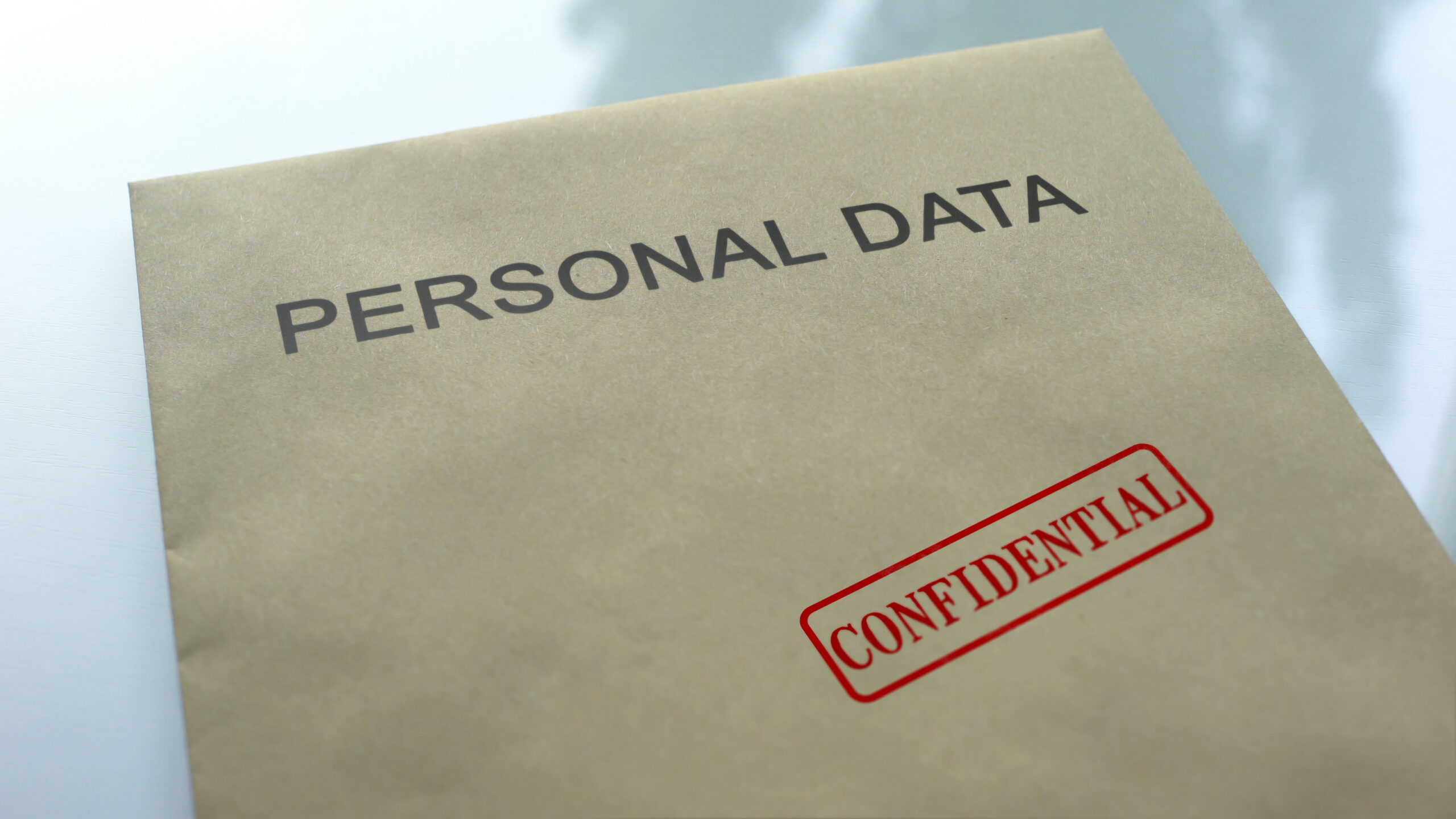 A manila envelope labeled 'PERSONAL DATA' with a red 'CONFIDENTIAL' stamp on it, placed on a reflective surface.