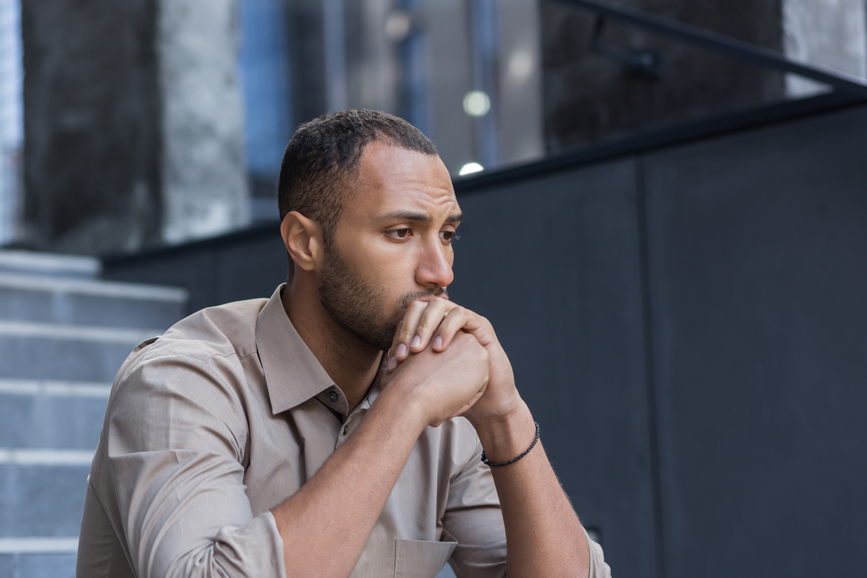 A contemplative man sitting on steps with his hands clasped, looking off into the distance.